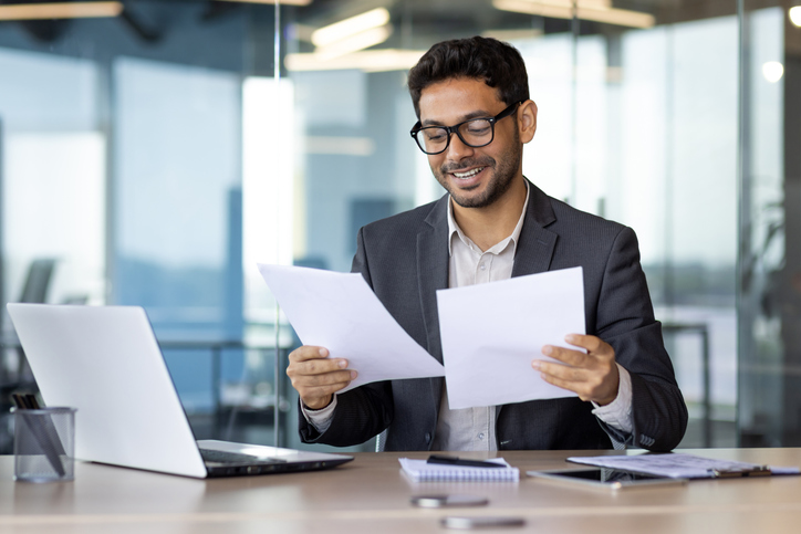 Successful mature experienced financier on paper work, Arab smiling satisfied with results of financial achievement, reviewing contracts, invoices and statements with accounts, businessman in suit