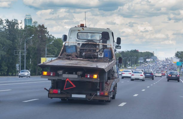 Tow Truck Carries a broken tow truck down a city street. Black car being dropped of at a mechanic by a tow truck